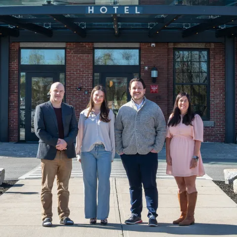 UNE business and Atlantic Hospitality leaders pose in front of the Biddeford skyline