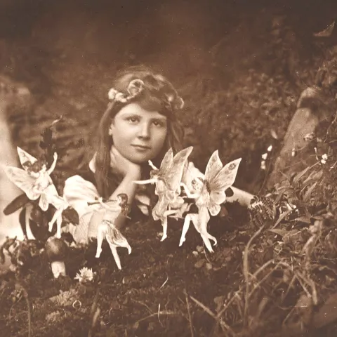 Sepia image of a girl in the woods surrounded by fairies