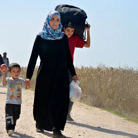 A woman walks down a dirt path with her children
