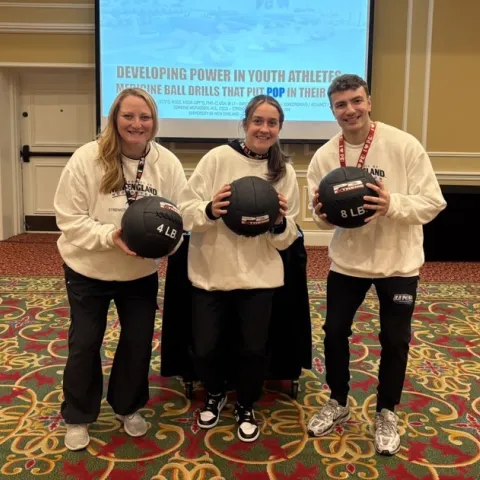 UNE student Aidan Curran poses with his research collaborators, all three are holding medicine balls