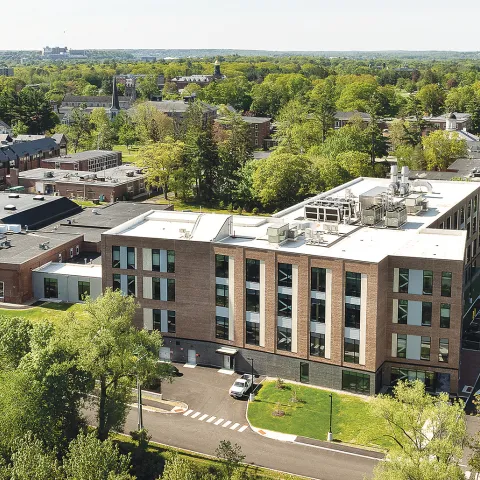 Aerial view of modern brick UNE health sciences campus building surrounded by trees and parking lots.