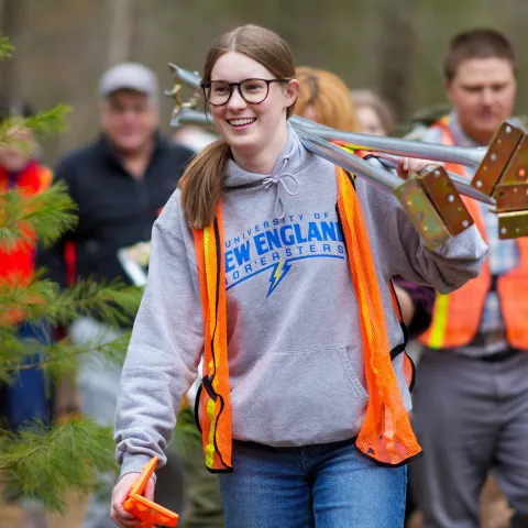 A UNE student carries research equipment through the woods